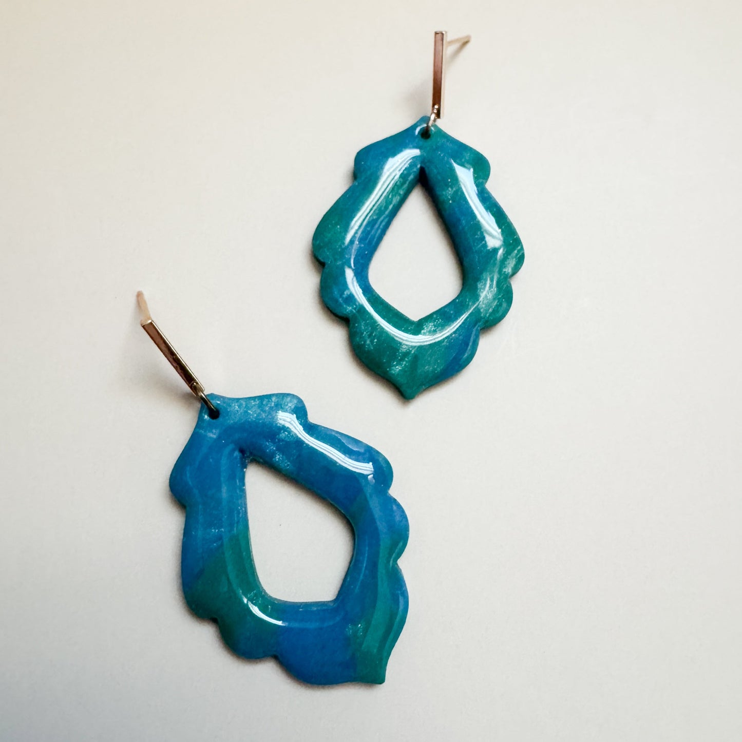 Pair of blue and green sparkling earrings on a light gray background