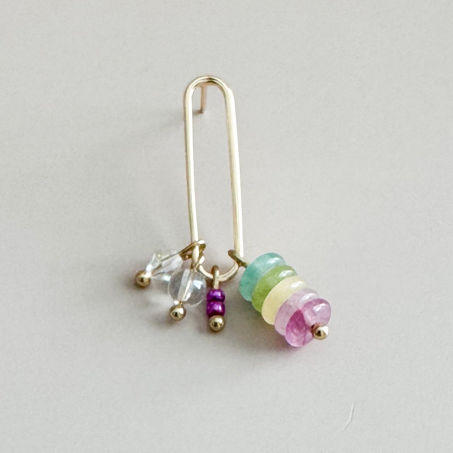 Gold earring with colorful beads on a light gray background