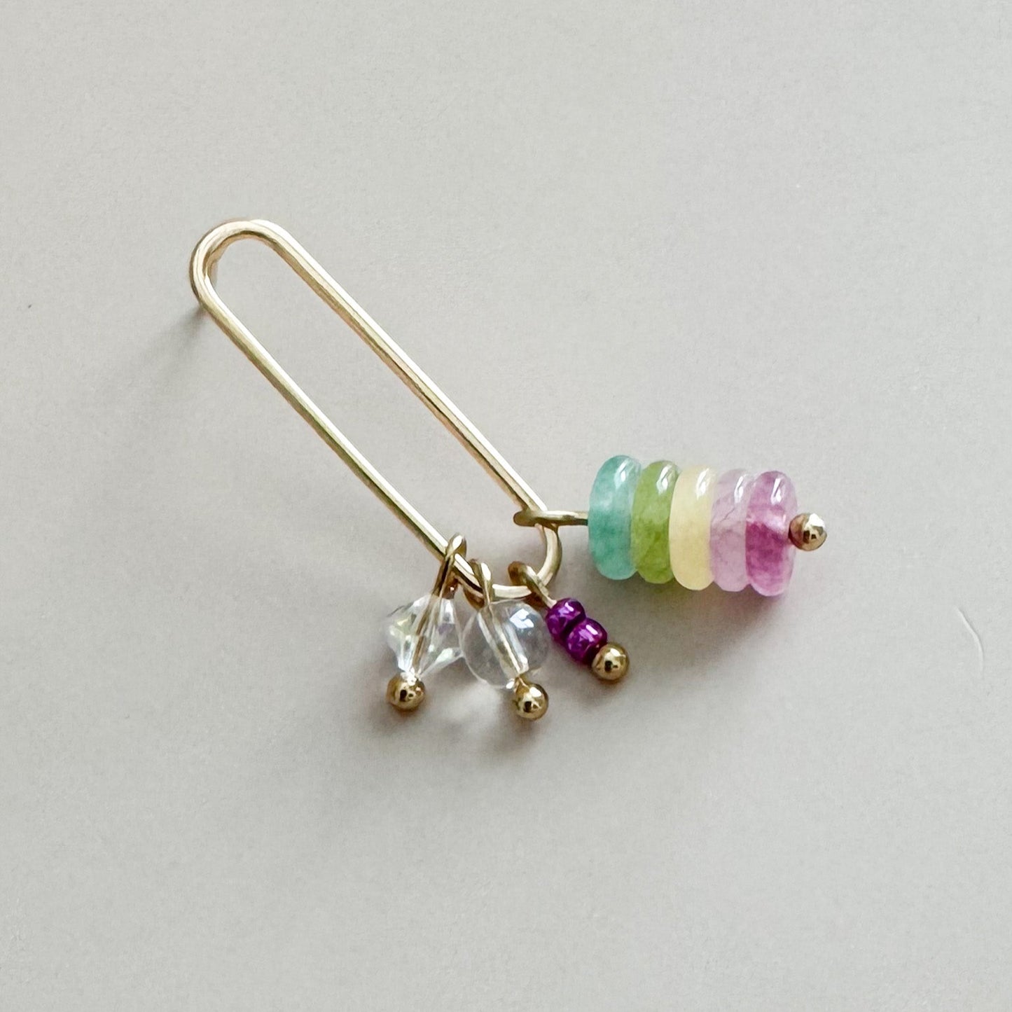 Gold earring with colorful beads on a light gray background