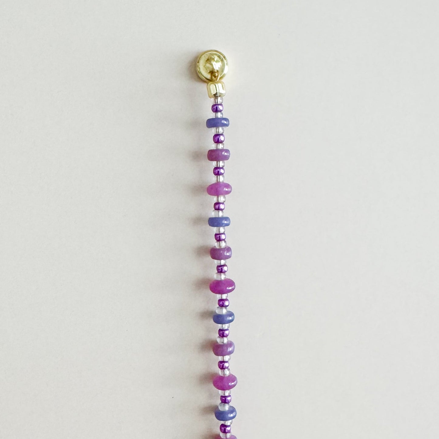 Beaded string with colorful beads and a gold clasp on a light gray background
