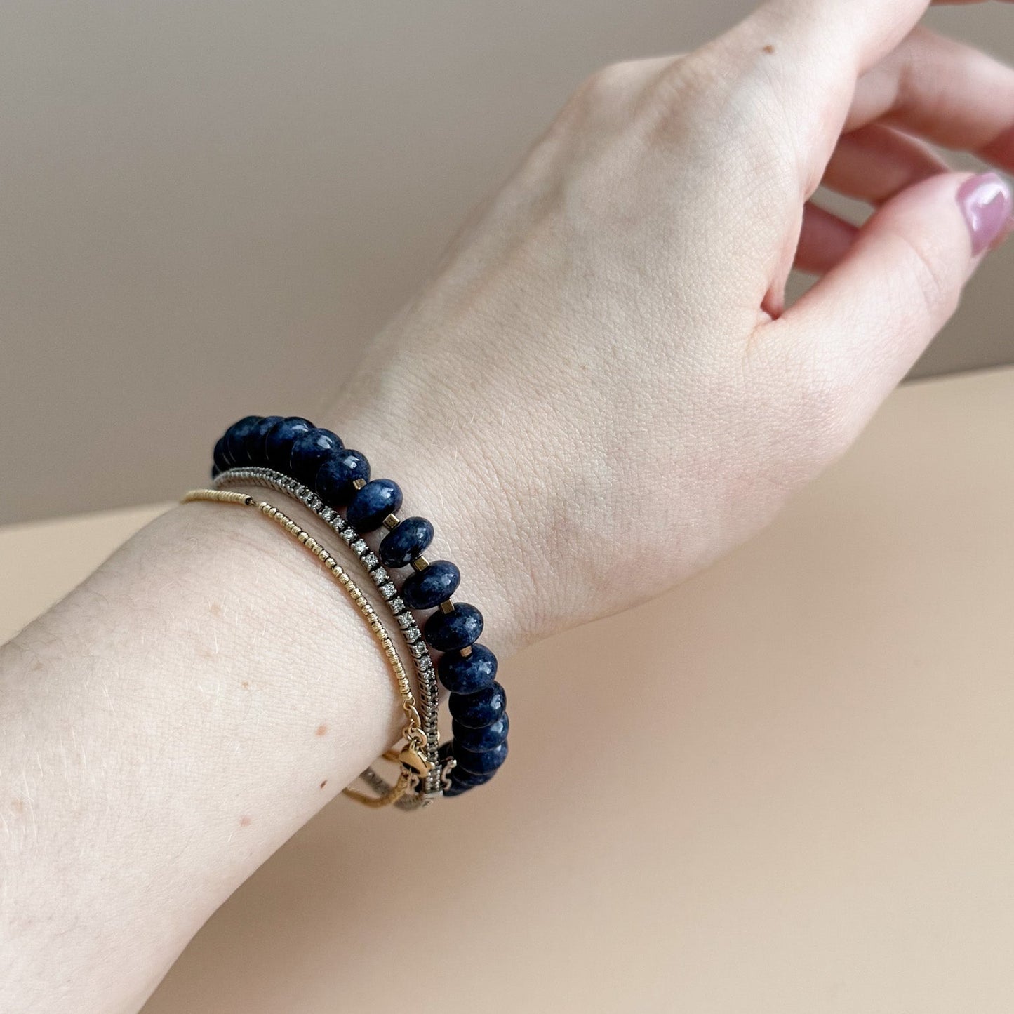 Hand wearing a navy blue beaded bracelet on a neutral background