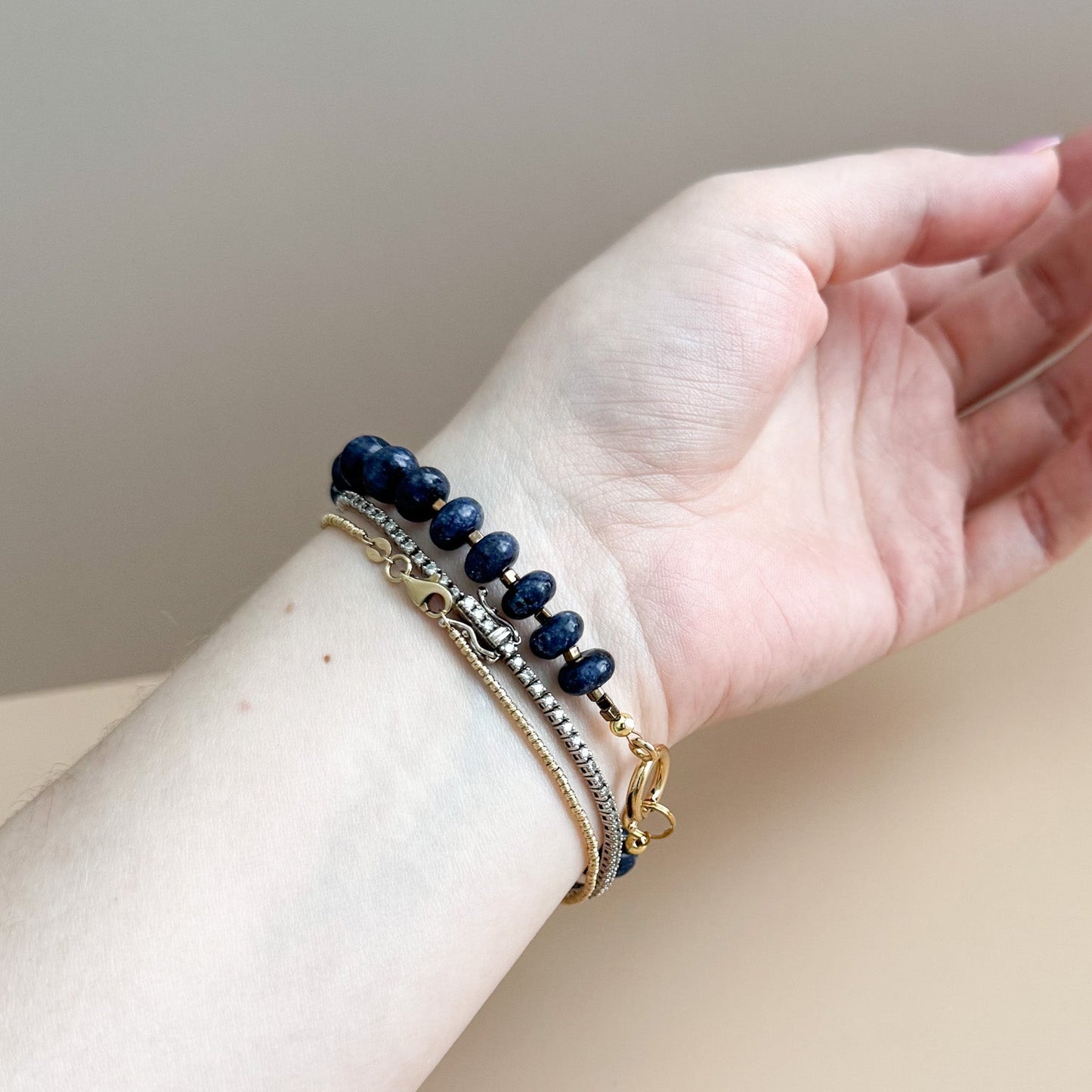Hand wearing a navy blue beaded bracelet on a neutral background