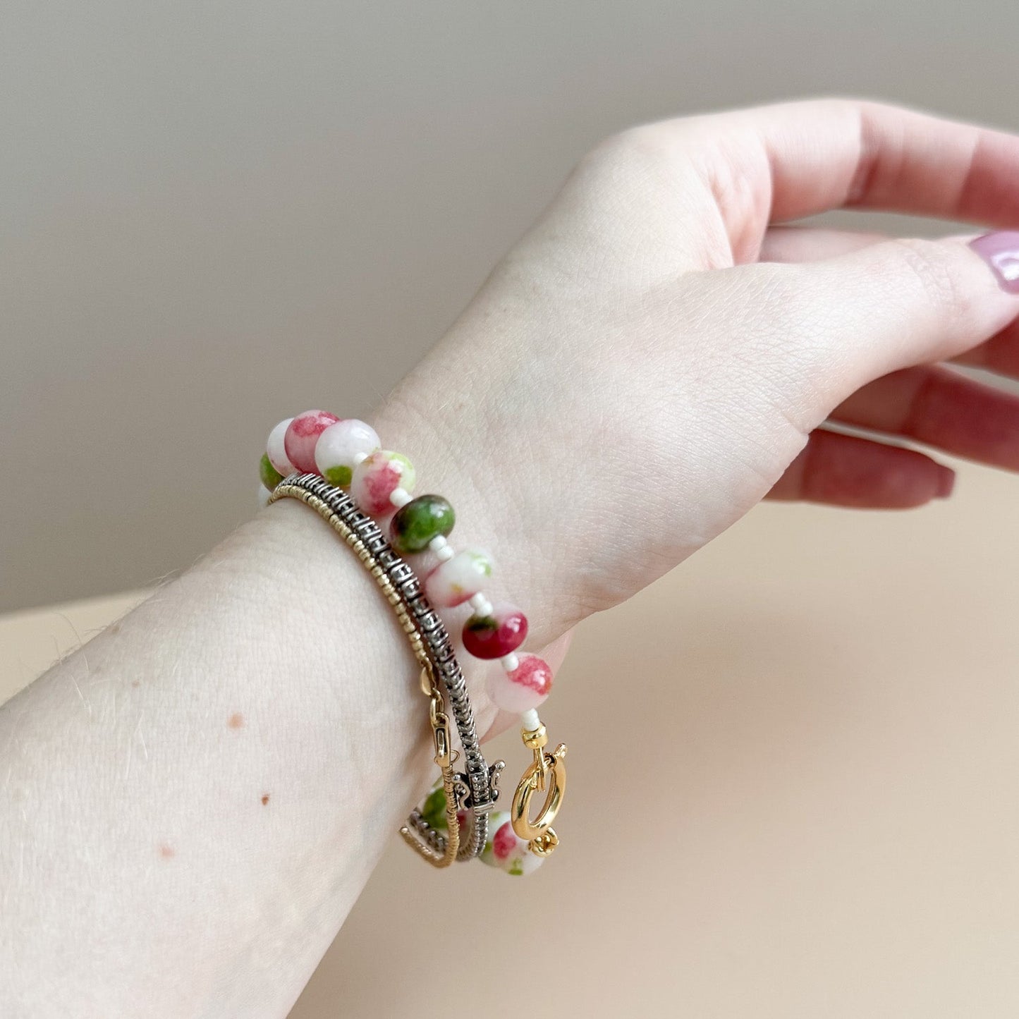 Hand wearing a bracelet with colorful beads on a neutral background