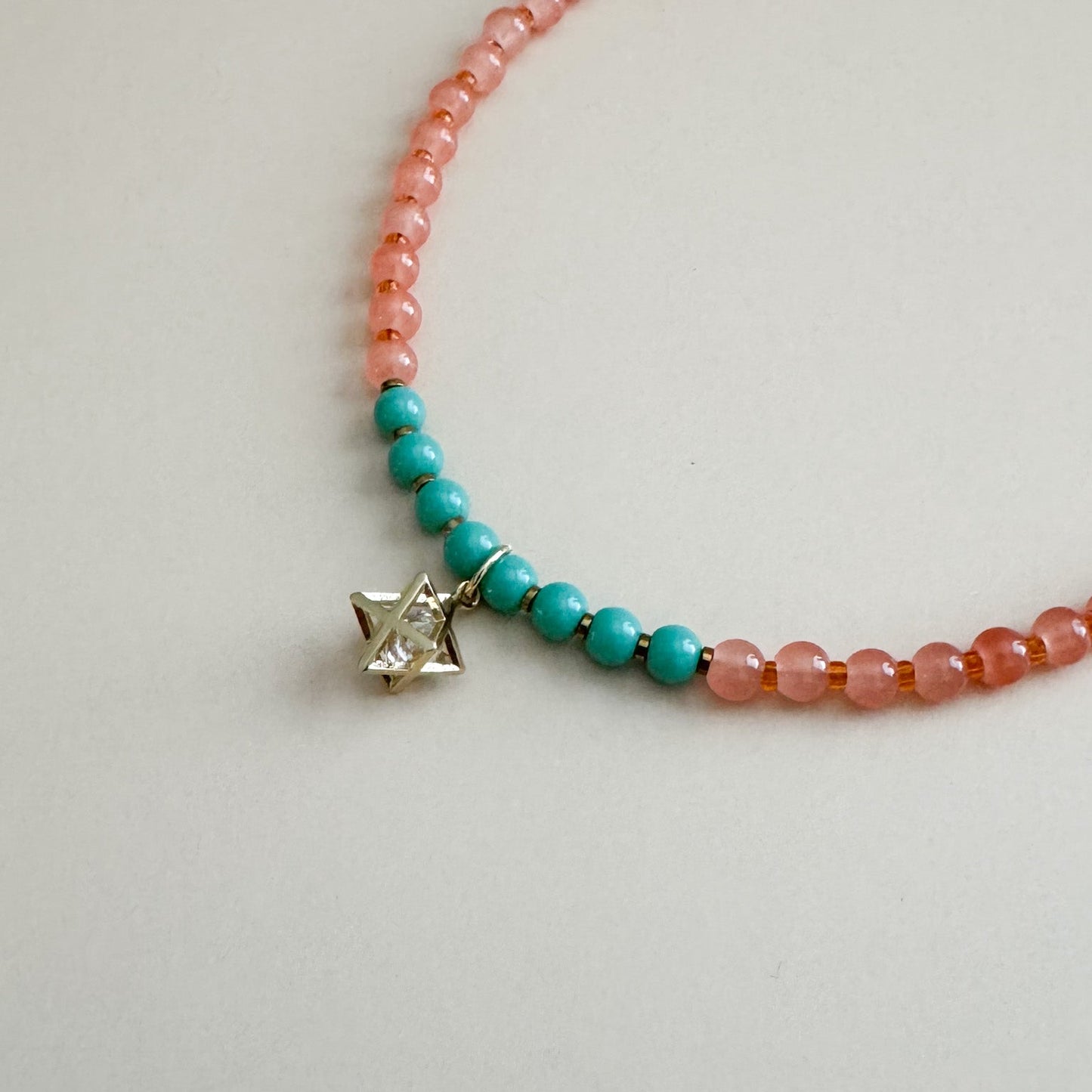 Mint green and translucent orange beaded necklace with a star-shaped charm on a light gray background