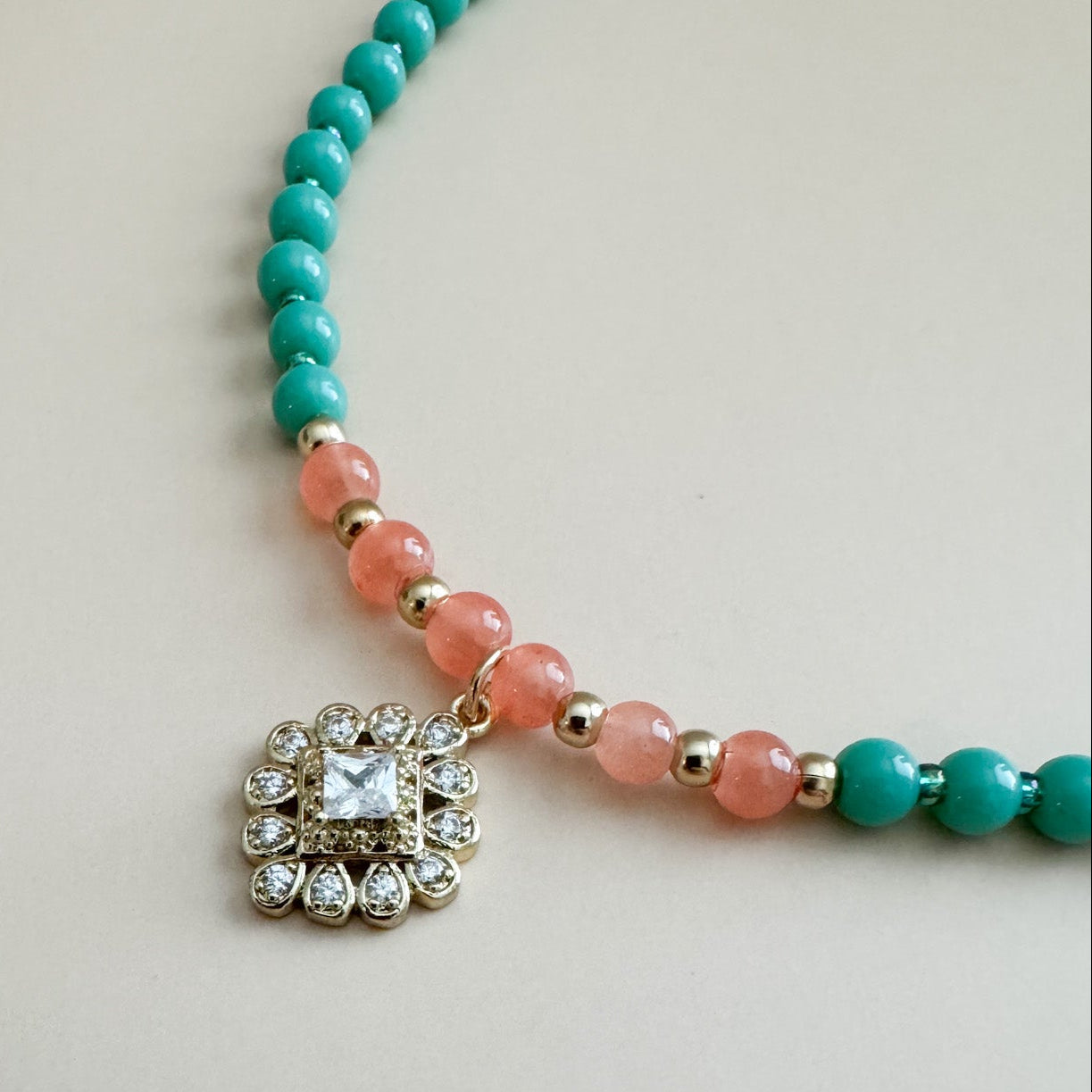 Mint green and translucent orange beaded bracelet with a decorative charm on a light background