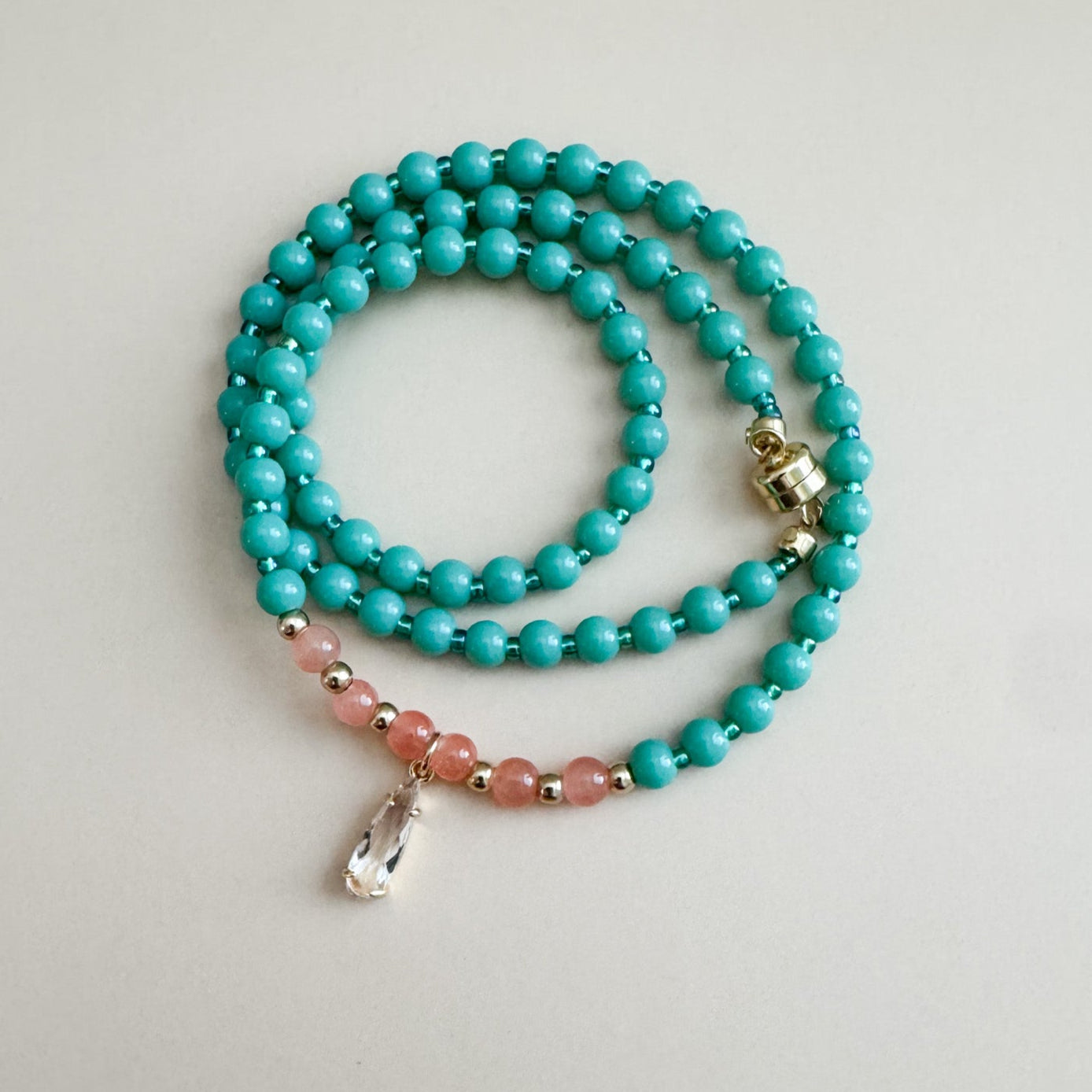 mint green and translucent orange beaded necklace with pink accents on a light gray background
