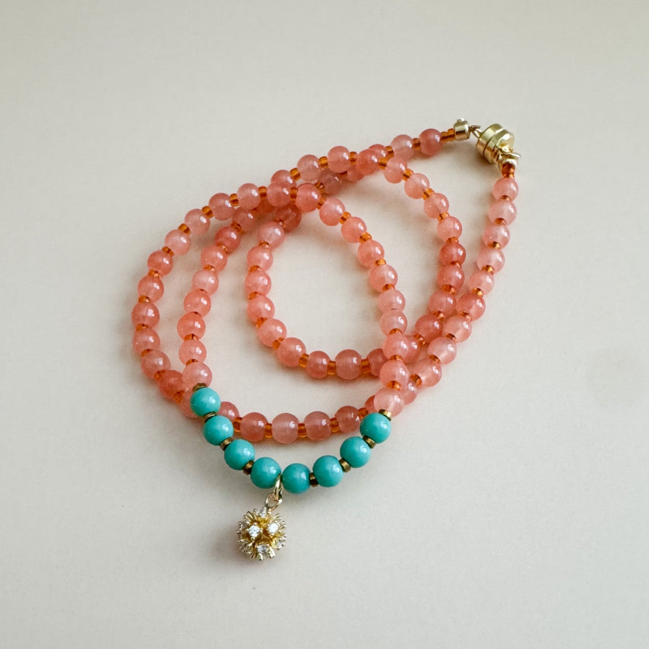 Beaded necklace with translucent orange and mint green beads on a light gray background