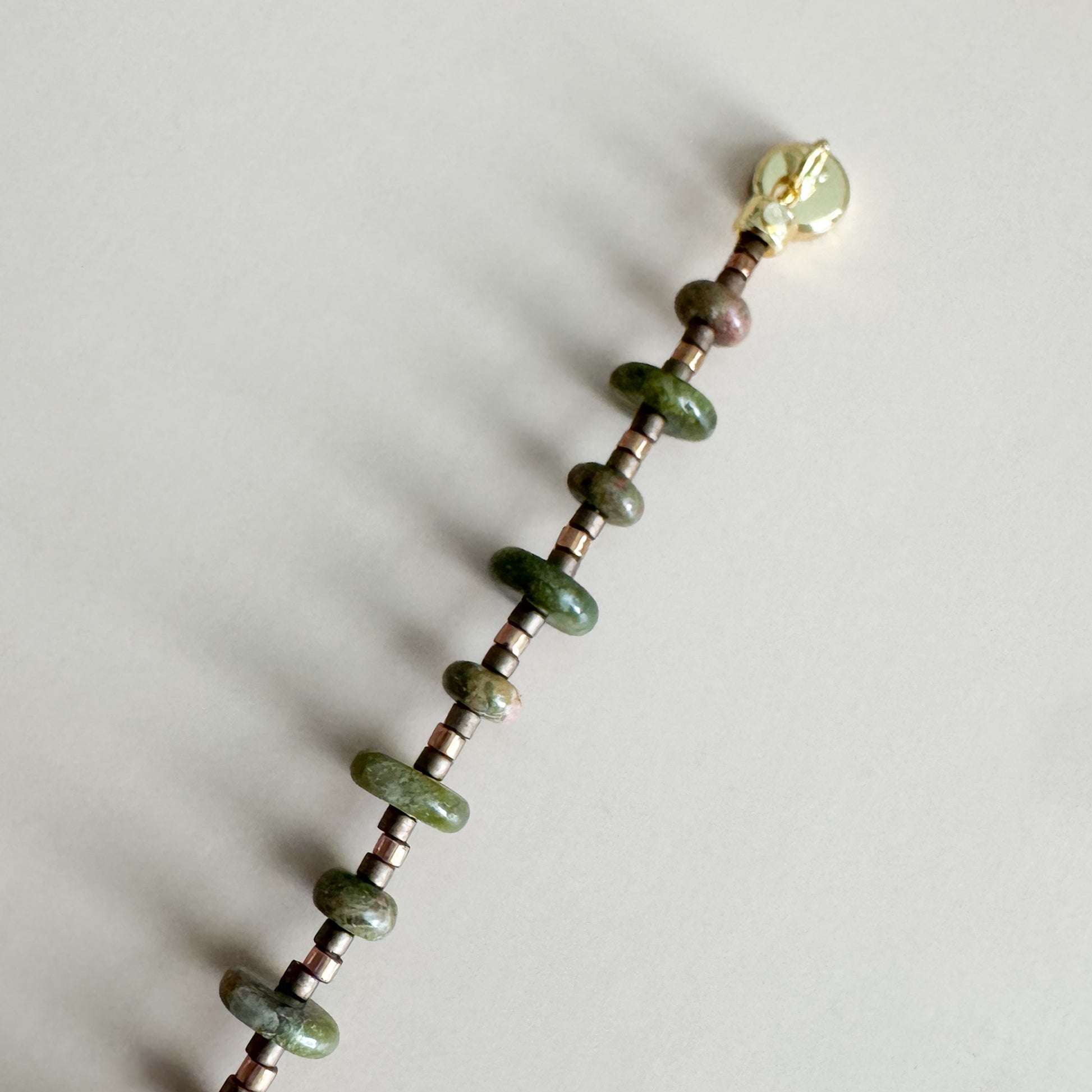 Beaded bracelet with unakite beads and a gold magnetic clasp on a light gray background