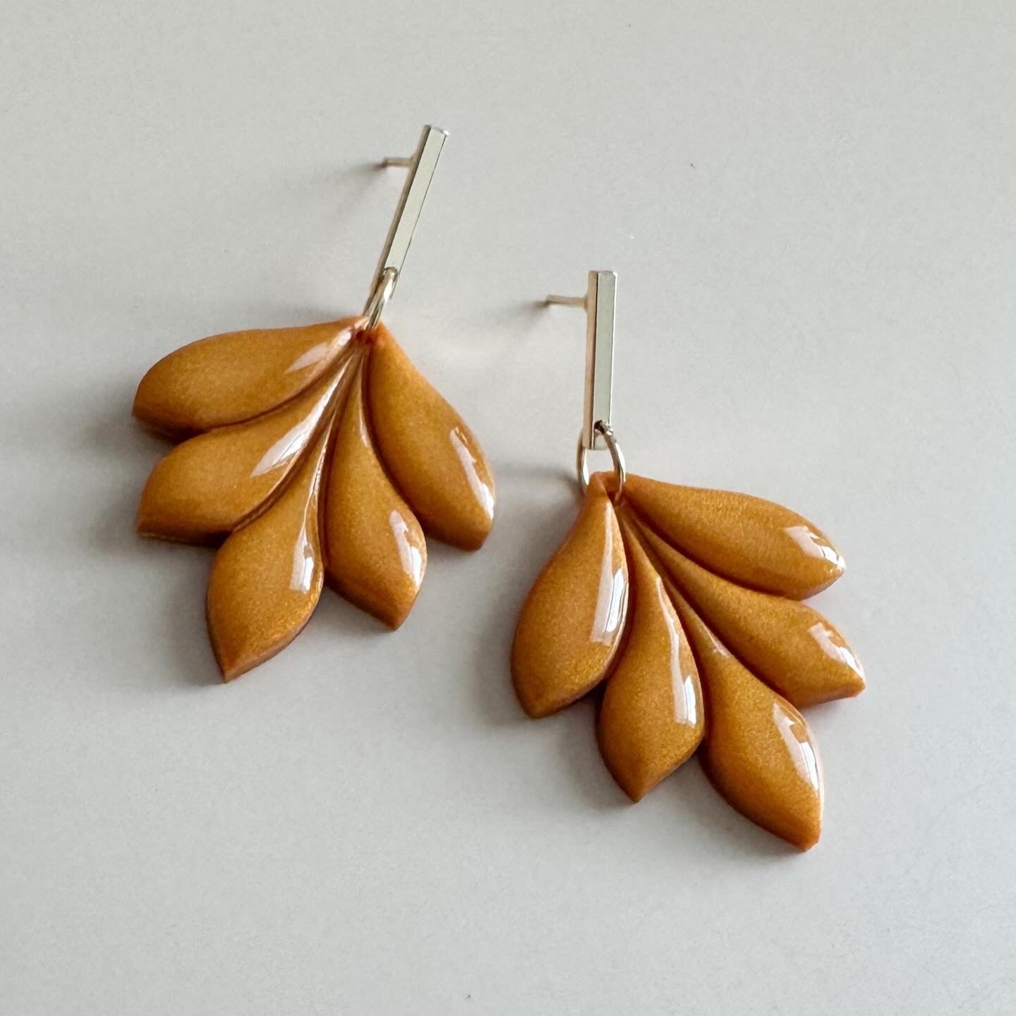 Pair of golden leaf-shaped earrings on a light gray background