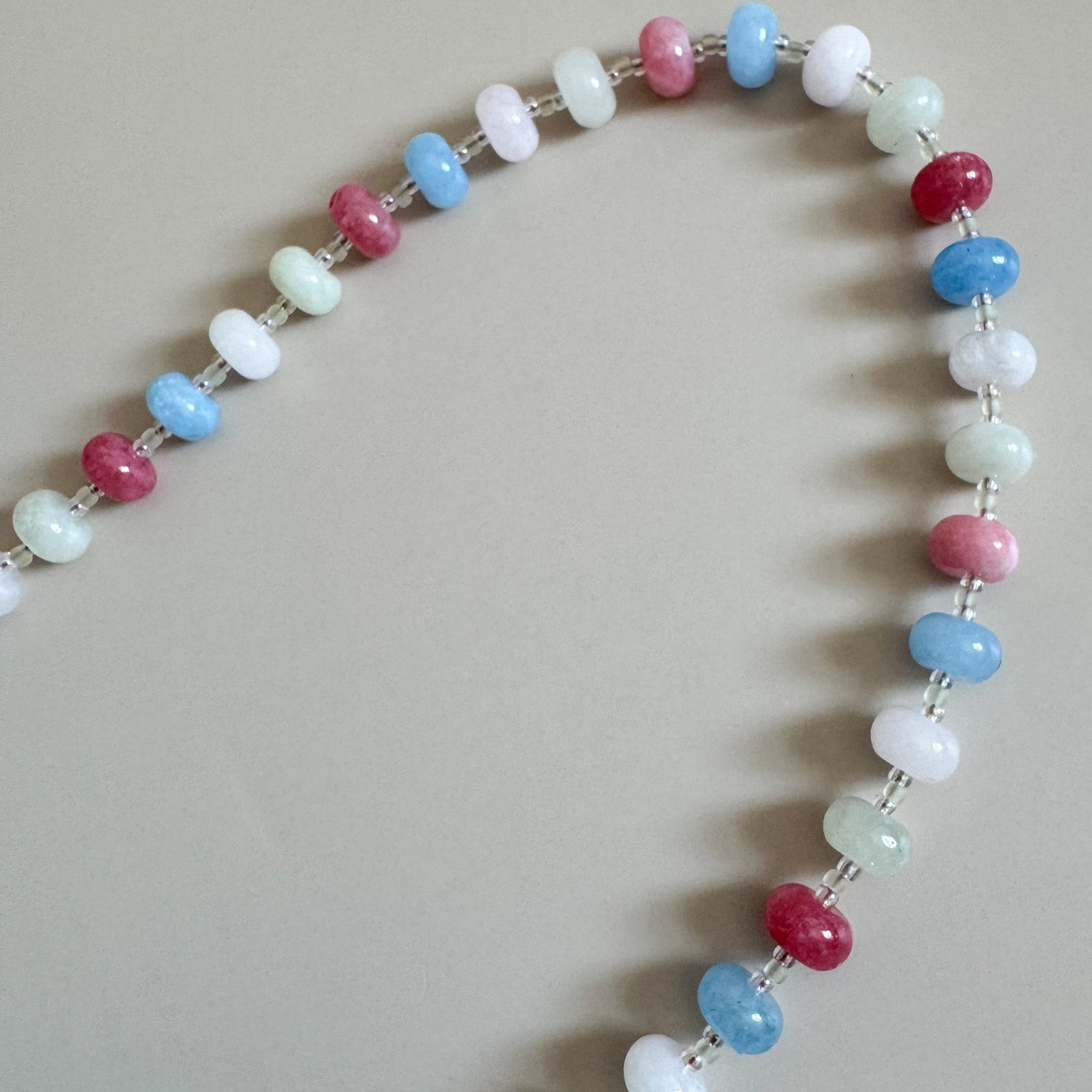 Lanyard with white, pale green, light blue, and shares of red beads on a plain background