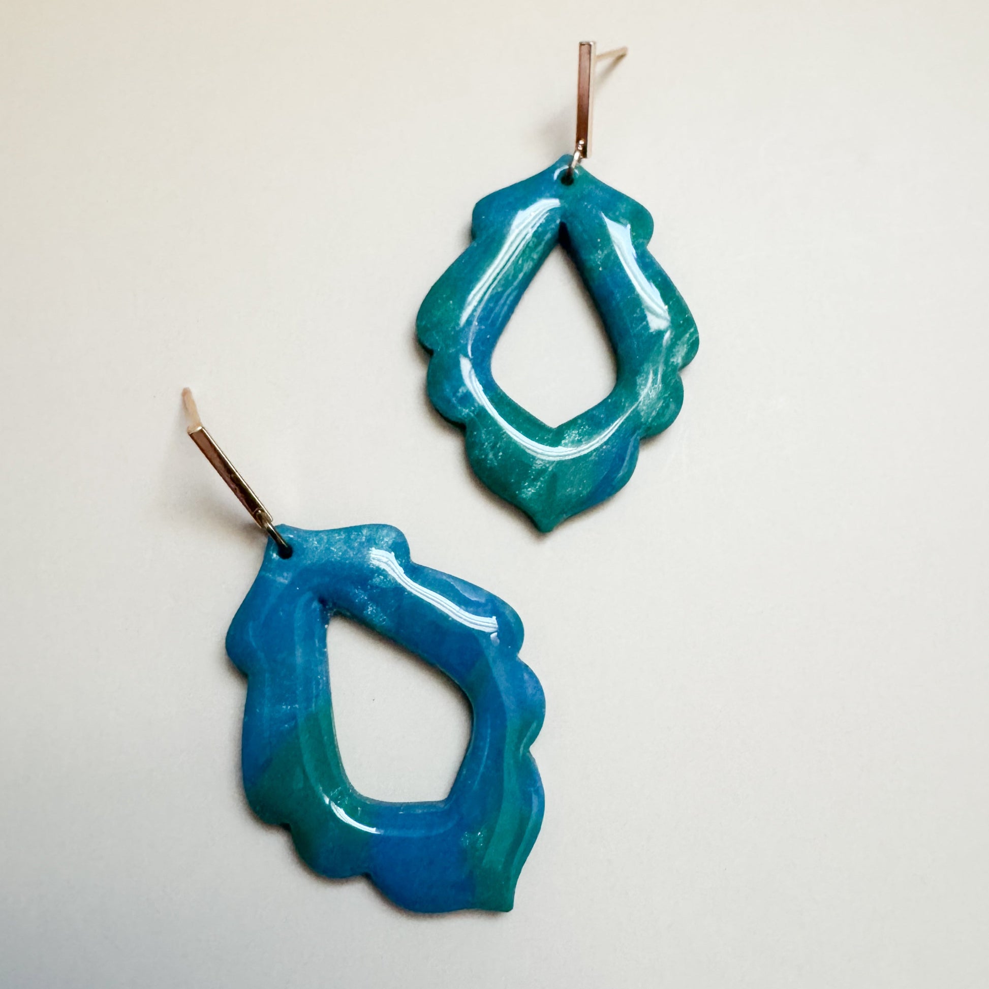 Pair of blue and green sparkling earrings on a light gray background