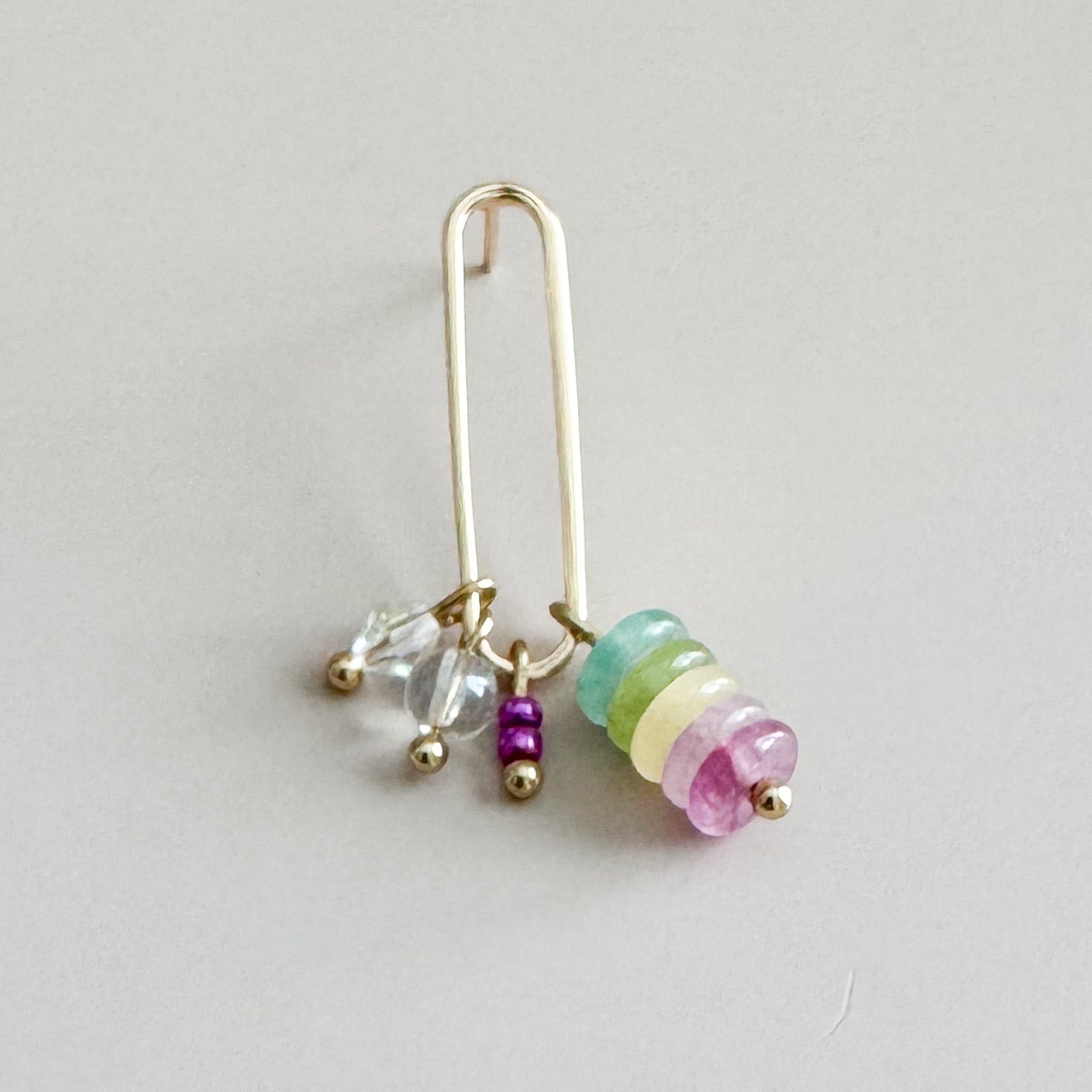 Gold earring with colorful beads on a light gray background