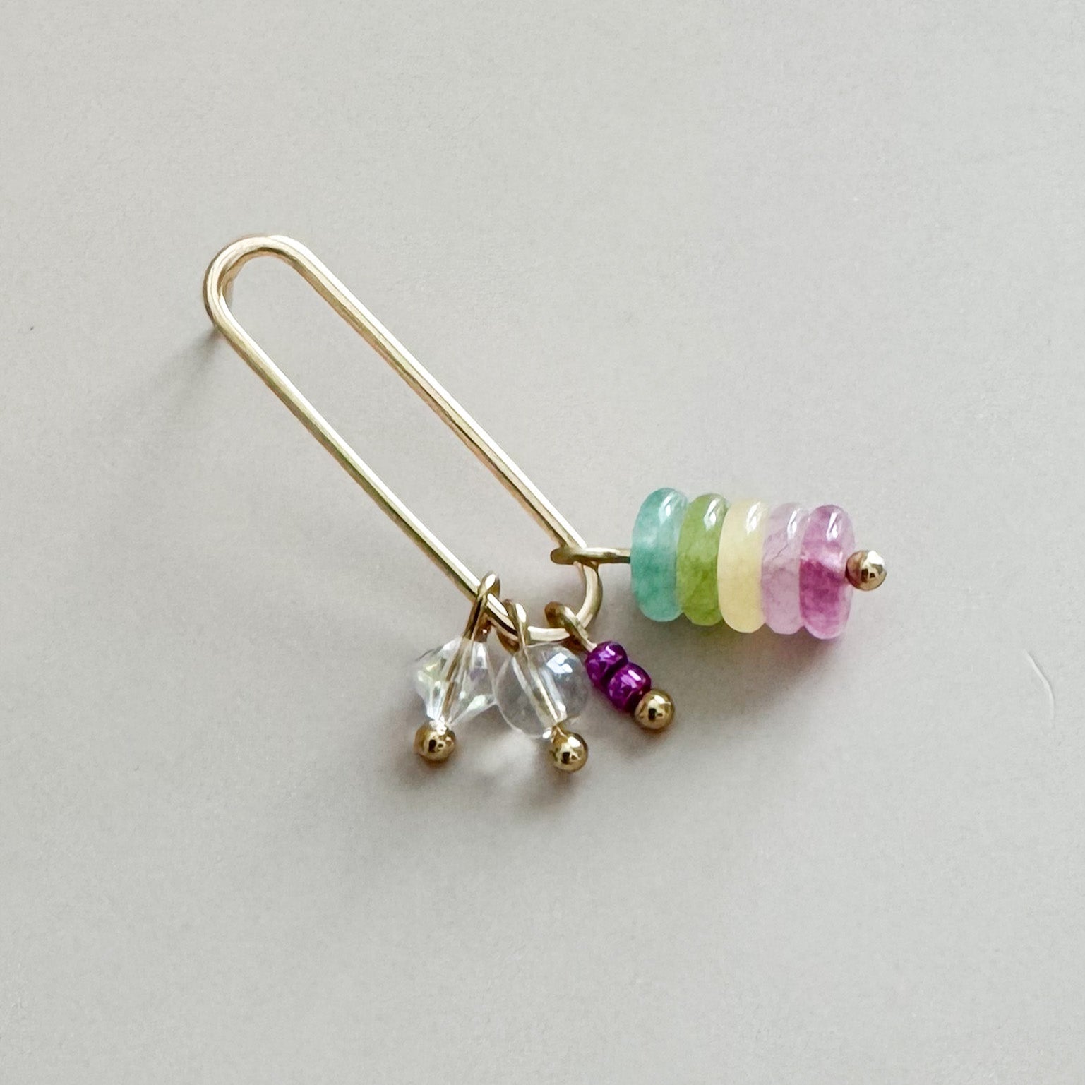 Gold earring with colorful beads on a light gray background