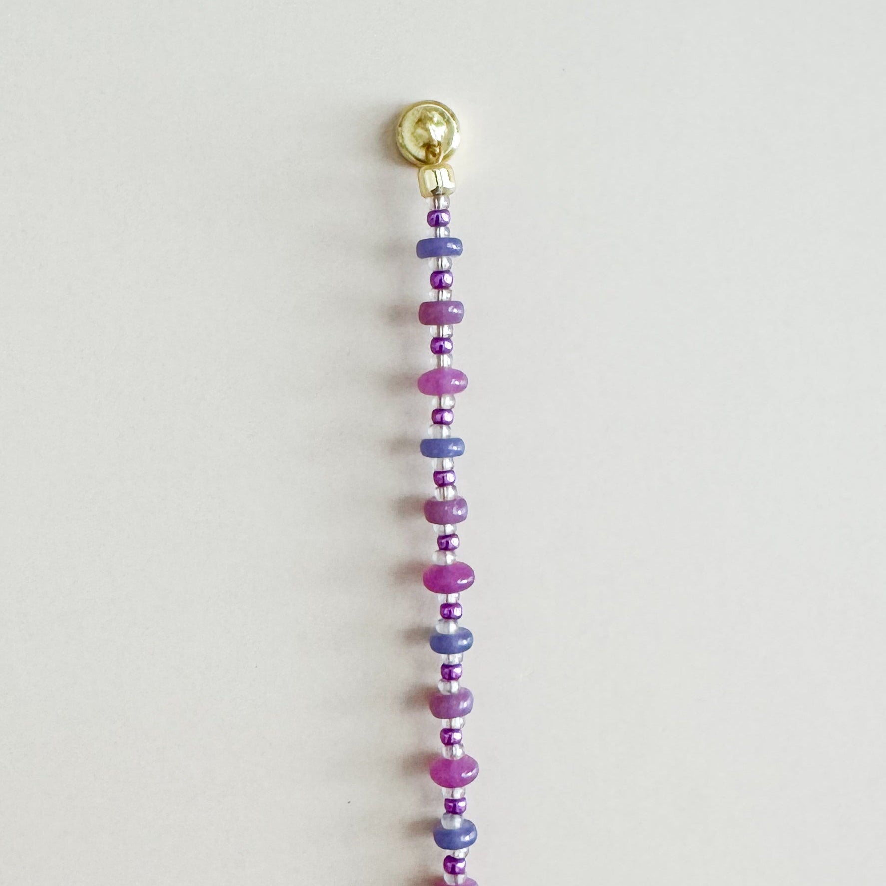 Beaded string with colorful beads and a gold clasp on a light gray background