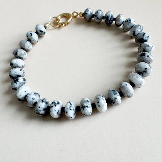 Bracelet with white, gray, and black speckled beads on a beige background
