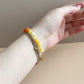 Hand wearing a bracelet with yellow beads on a neutral background