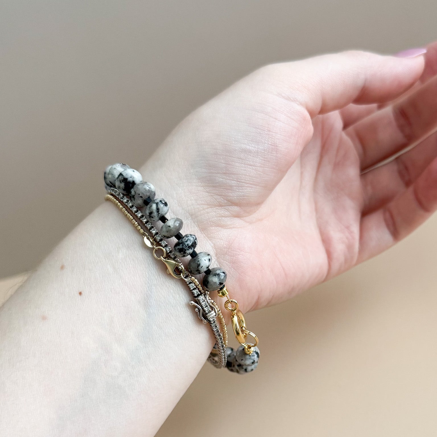 Hand wearing a bracelet with white, black, and gray beads on a neutral background