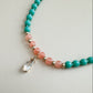 Beaded necklace with mint green and translucent orange beads with an elongated teardrop gem on a light gray background