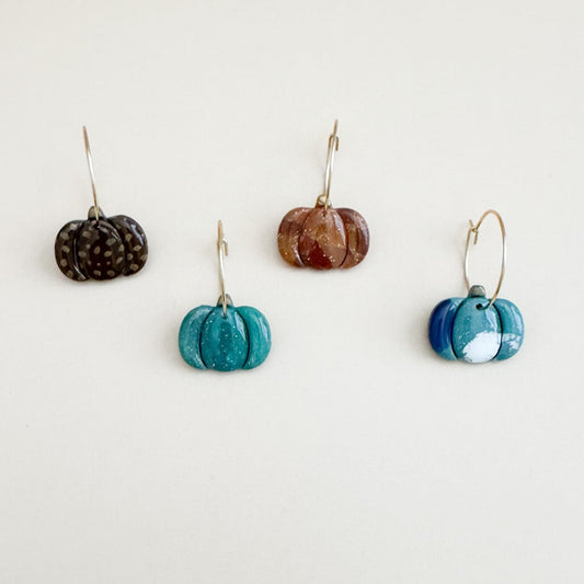 Four pumpkin earrings with different designs on a white background